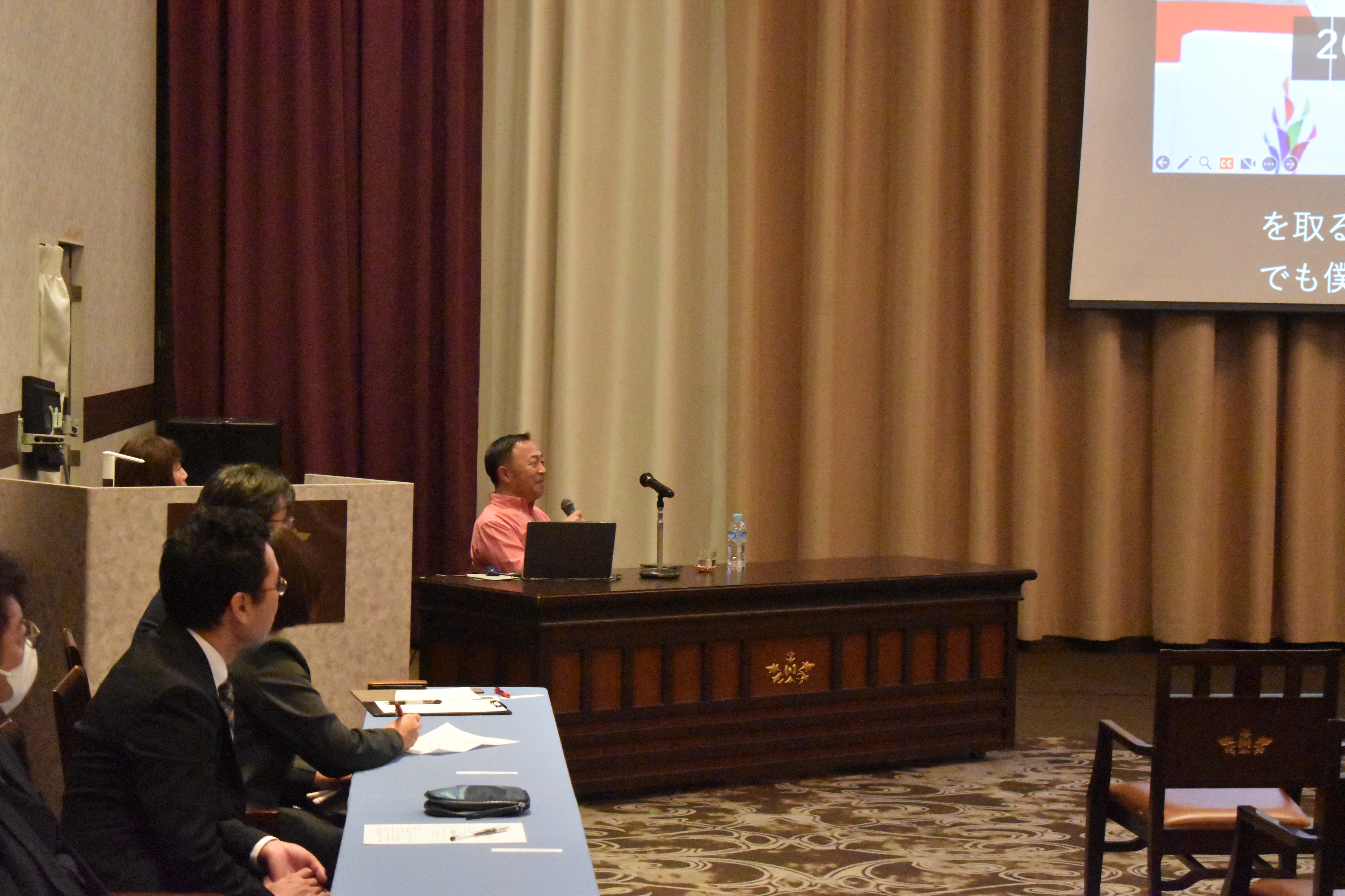 写真：会場前方のスクリーンに発表スライドが映し出され、参加者が前方を見つめている様子