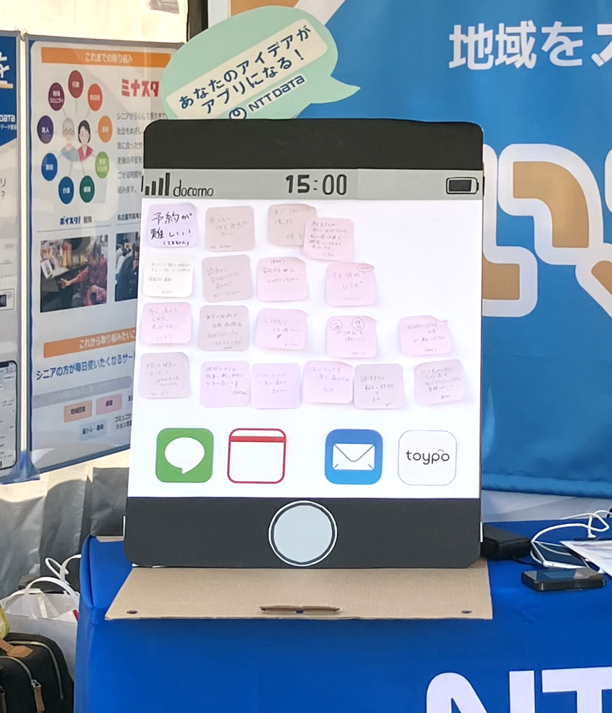 写真：スマホ型パネルに手書き付箋が貼られ、アプリ開発アイデアを募集する展示