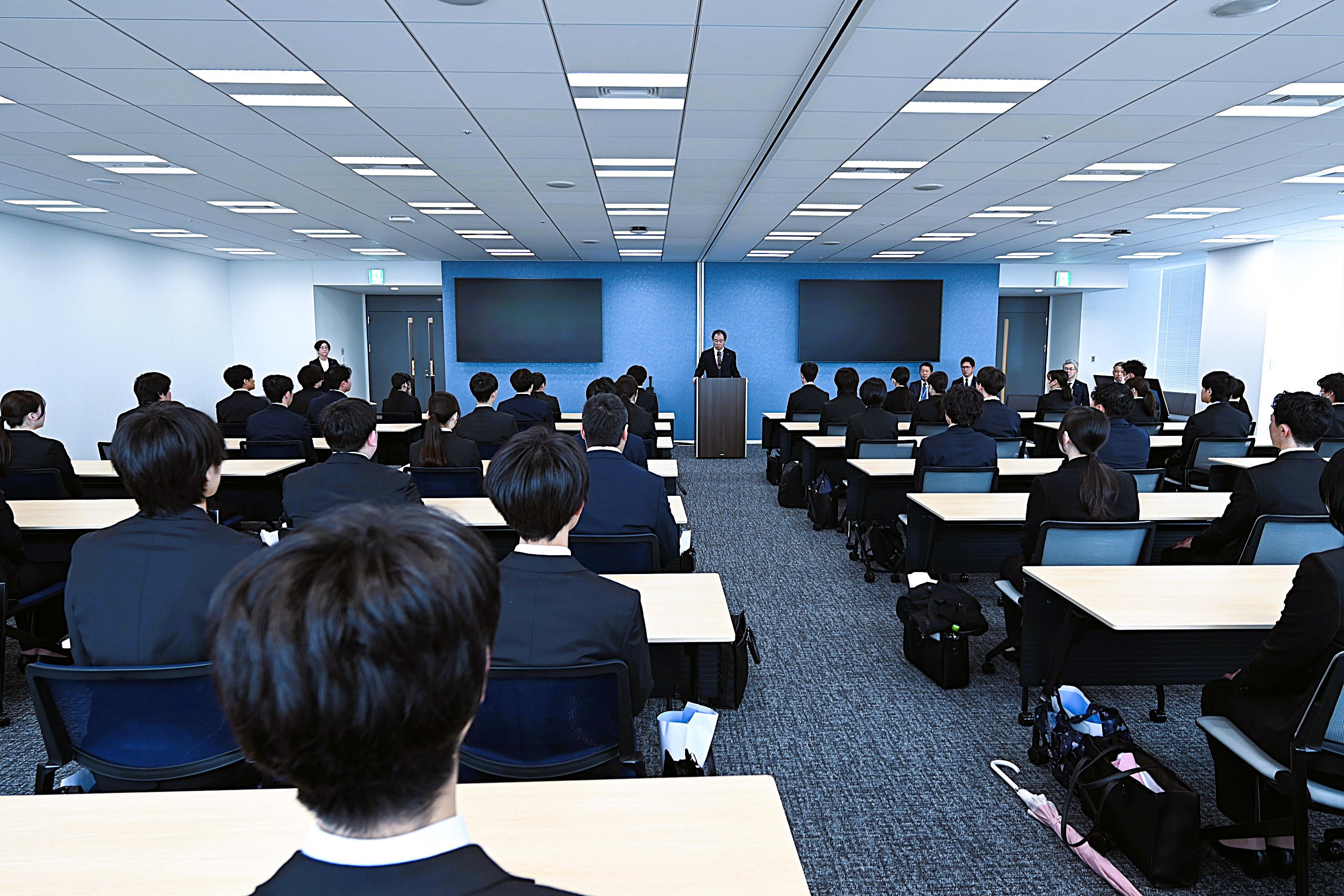写真：2026年度入社式の会場で、社長が新入社員を前に歓迎の挨拶を述べている場面